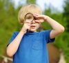 A young white boy with blond hair looking through a magnifying glass.